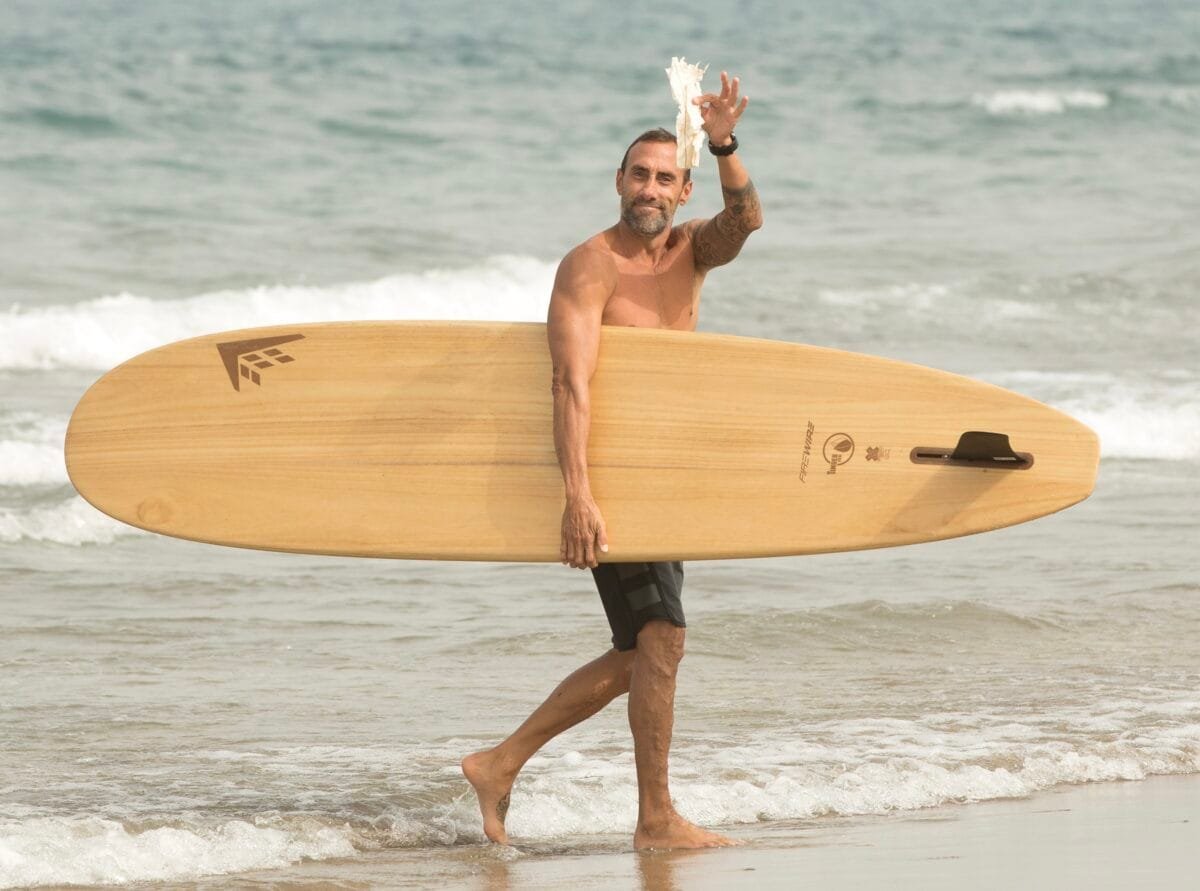 Surfer agarrando botella de plástico saliendo del mar